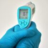 Close-up of an infrared thermometer held by hands in blue disposable gloves.