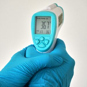 Close-up of an infrared thermometer held by hands in blue disposable gloves.